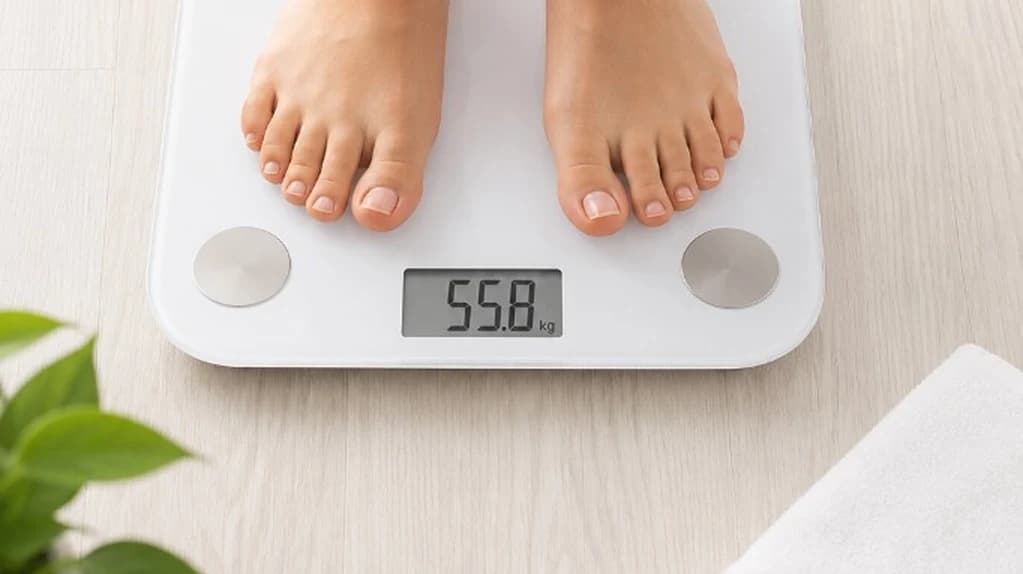 Bare feet stepping onto a sleek white body-composition scale in a calm, sunlit studio — Weightloss & body care at The Wellness Ed.