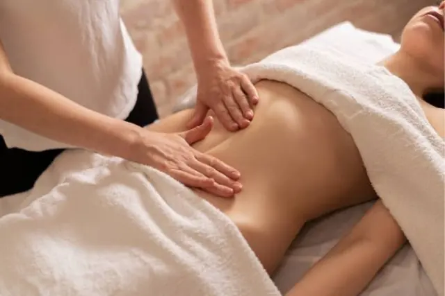 Close-up of a Lymphatic Drainage session at The Wellness Ed — a therapist's hands glide in light, precise, rhythmic strokes across a guest's oiled back, supporting the body's natural fluid balance.