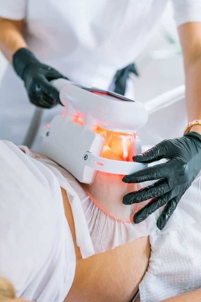 Clinician in black gloves carefully positioning the CoolSculpt cryolipolysis applicator on a guest's abdomen during a body contouring session at The Wellness Ed — the cooling cup is engaged on the targeted fat pocket while the guest reclines comfortably.