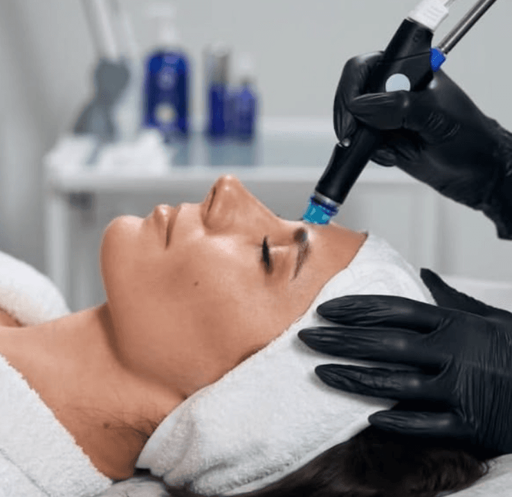 A relaxed client receiving a Hydrafacial treatment at The Wellness Ed Signature Studio, with a clinician in black gloves gently guiding the Hydrafacial wand across her forehead.