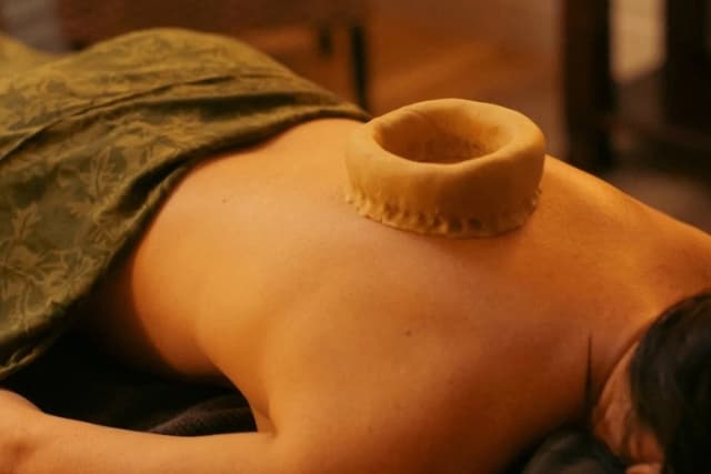 Close-up of a Kati Basti (Abdominal Focus) therapy at The Wellness Ed — a hand-shaped dough ring is set on a guest's lower back and pooled with warm medicated oil, the warm-lit room reflecting the ritual's grounded, restorative cadence.