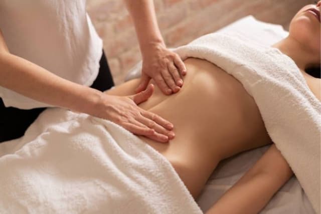 Close-up of a Lymphatic Drainage session at The Wellness Ed — a therapist's hands glide in light, precise, rhythmic strokes across a guest's oiled back, supporting the body's natural fluid balance.